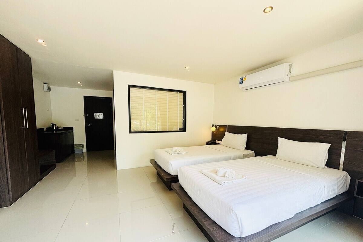 A hotel room with two beds, a wardrobe, a bathroom, and a large window.