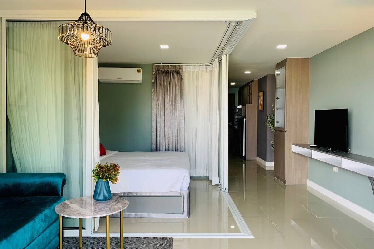 A modern hotel room with a bed, a TV, a small table, and a sofa.