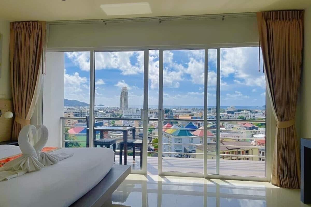 A hotel room with a large sliding glass door leading to a balcony, offering a city view.