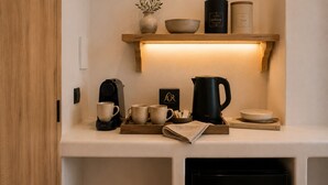 A kitchen area with a coffee maker, mugs, a kettle, and a shelf with containers labeled 'Coffee' and 'Tea'. - Aegeeis (Santorini)