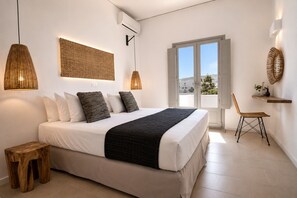 Une chambre à coucher avec un lit, des lampes de chevet, un petit tabouret en bois, une chaise en osier et une fenêtre donnant sur un beau paysage.