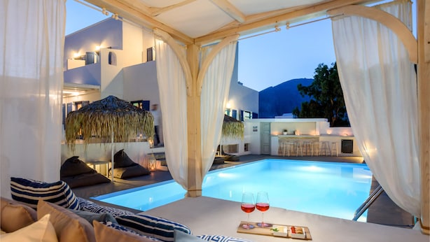A luxurious poolside area with a bed, pillows, and two glasses of red wine on a tray. - Aegeeis (Santorini)
