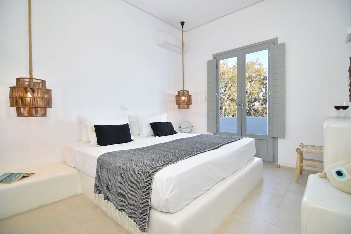 A bedroom with a bed, bedside tables, a window with shutters, and a hanging light fixture.