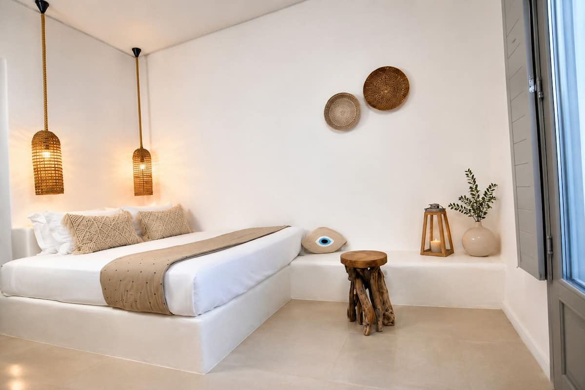 A modern bedroom with a large bed, two hanging light fixtures, a small round table, and a window with a view.