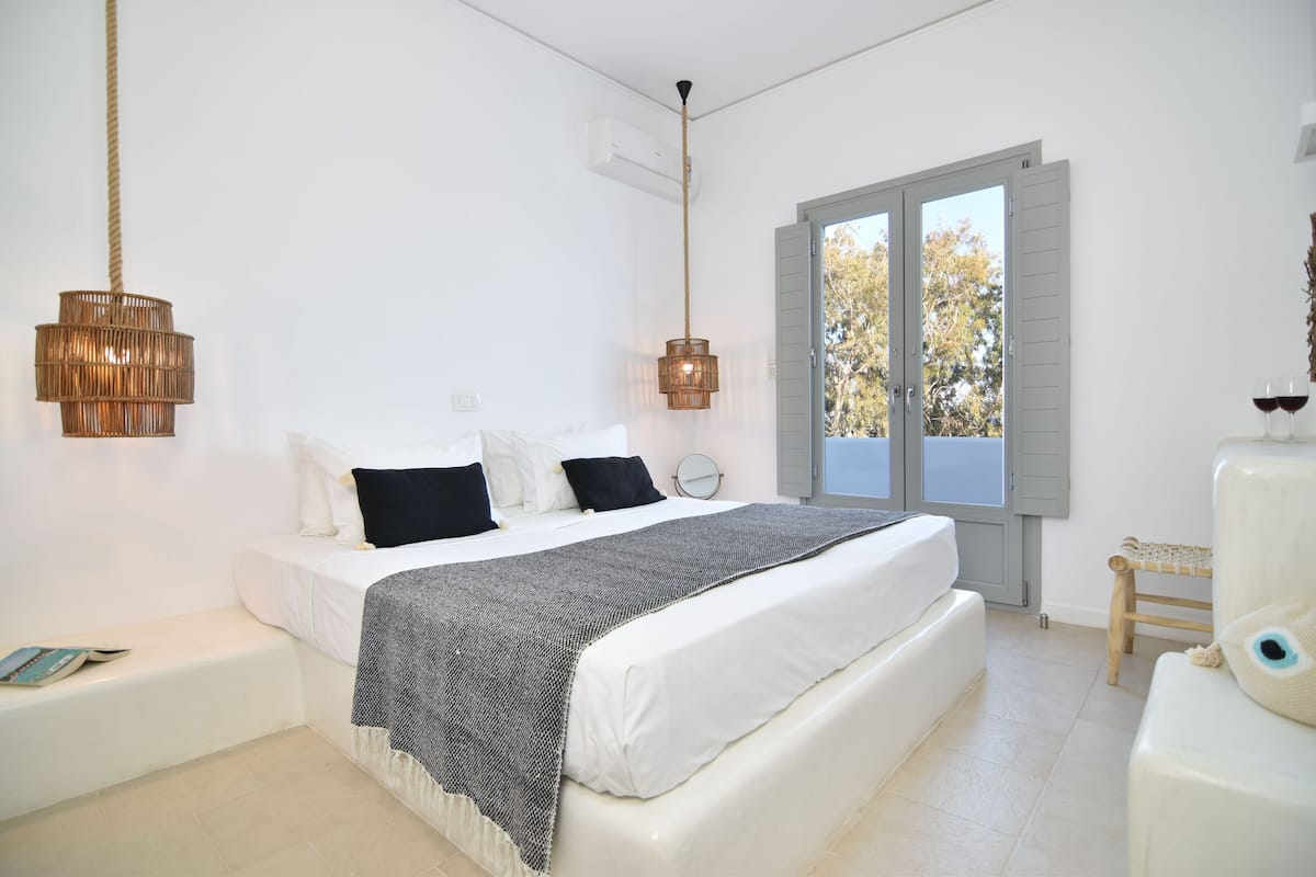 A bedroom with a bed, bedside tables, a window with shutters, and a hanging light fixture.