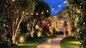 Un sendero lleva a una casa con luces colgantes y vegetación.