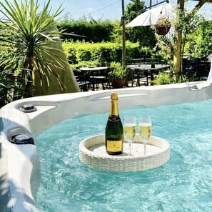 A hot tub with a bottle of champagne and two glasses on a floating tray. - Duck Lodge B&B (Brighton)