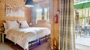 Un dormitorio de cabaña de madera con una cama, una lámpara colgante, un extintor y vistas al exterior.