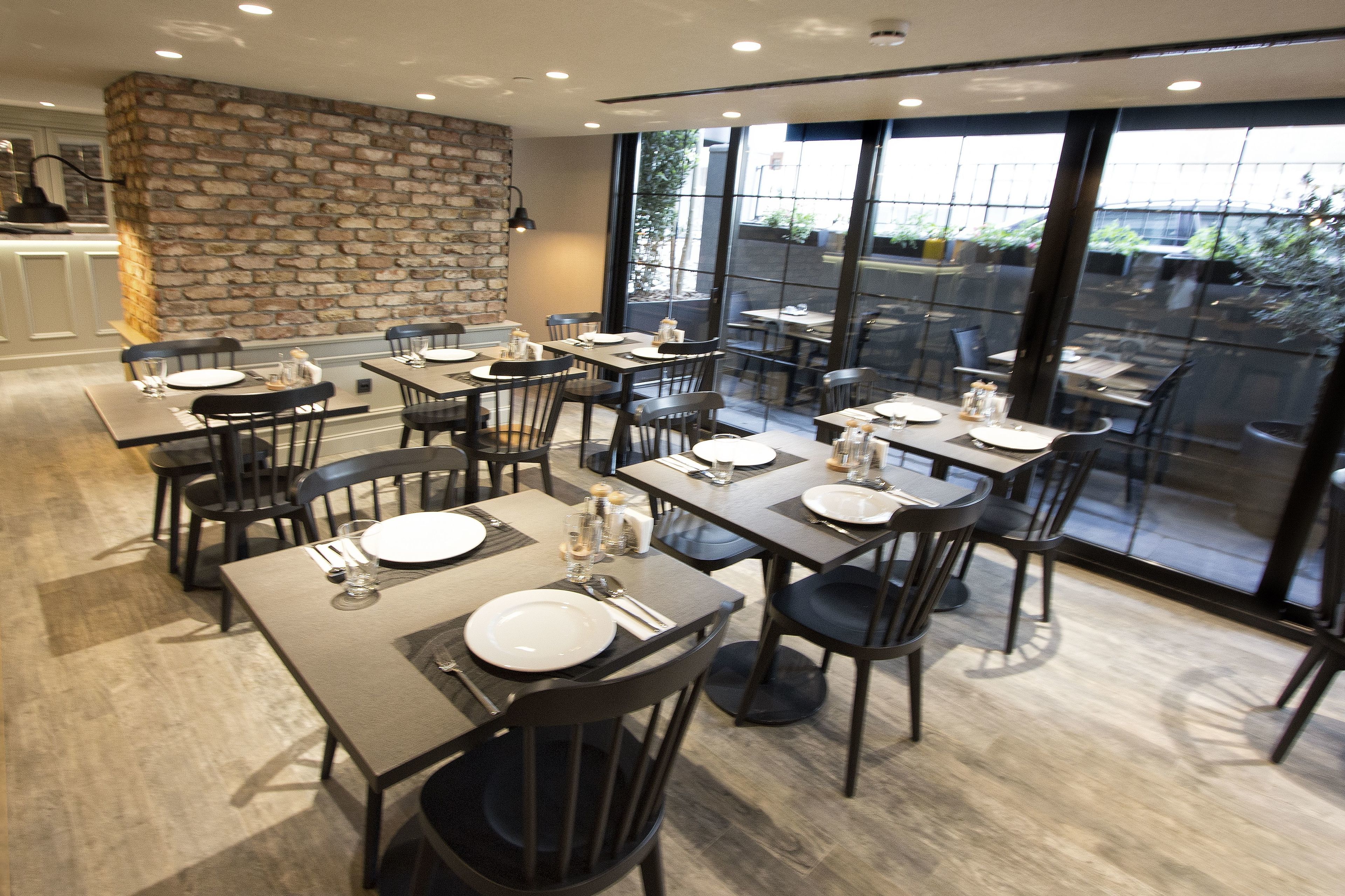 Un restaurante con mesas dispuestas para comer, una pared de piedra y grandes ventanales con vistas.
