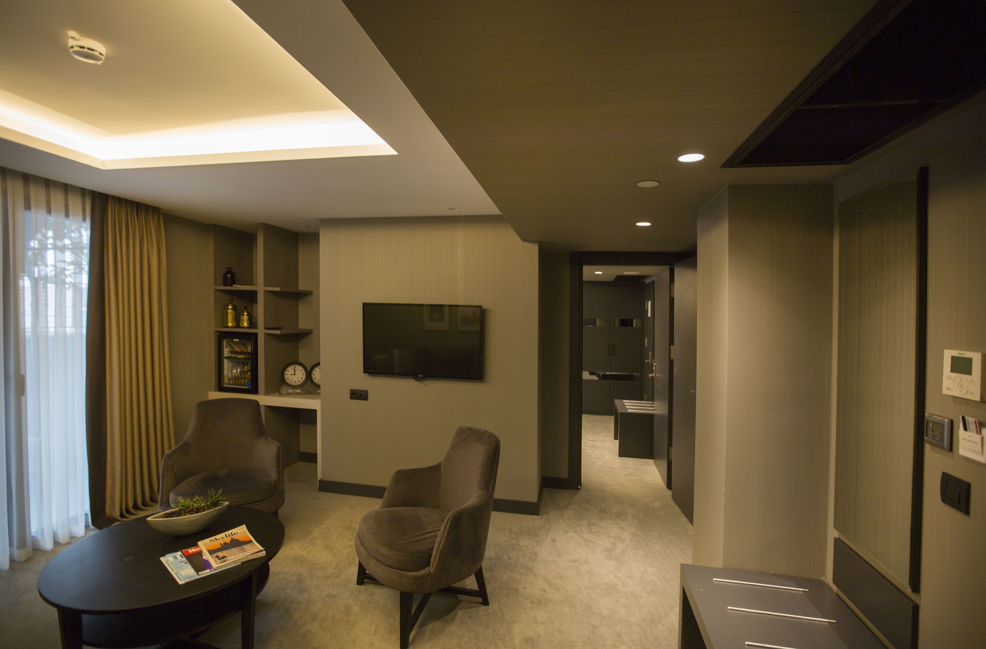 A modern hotel room with a flat-screen TV, two armchairs, a coffee table, and a small side table.