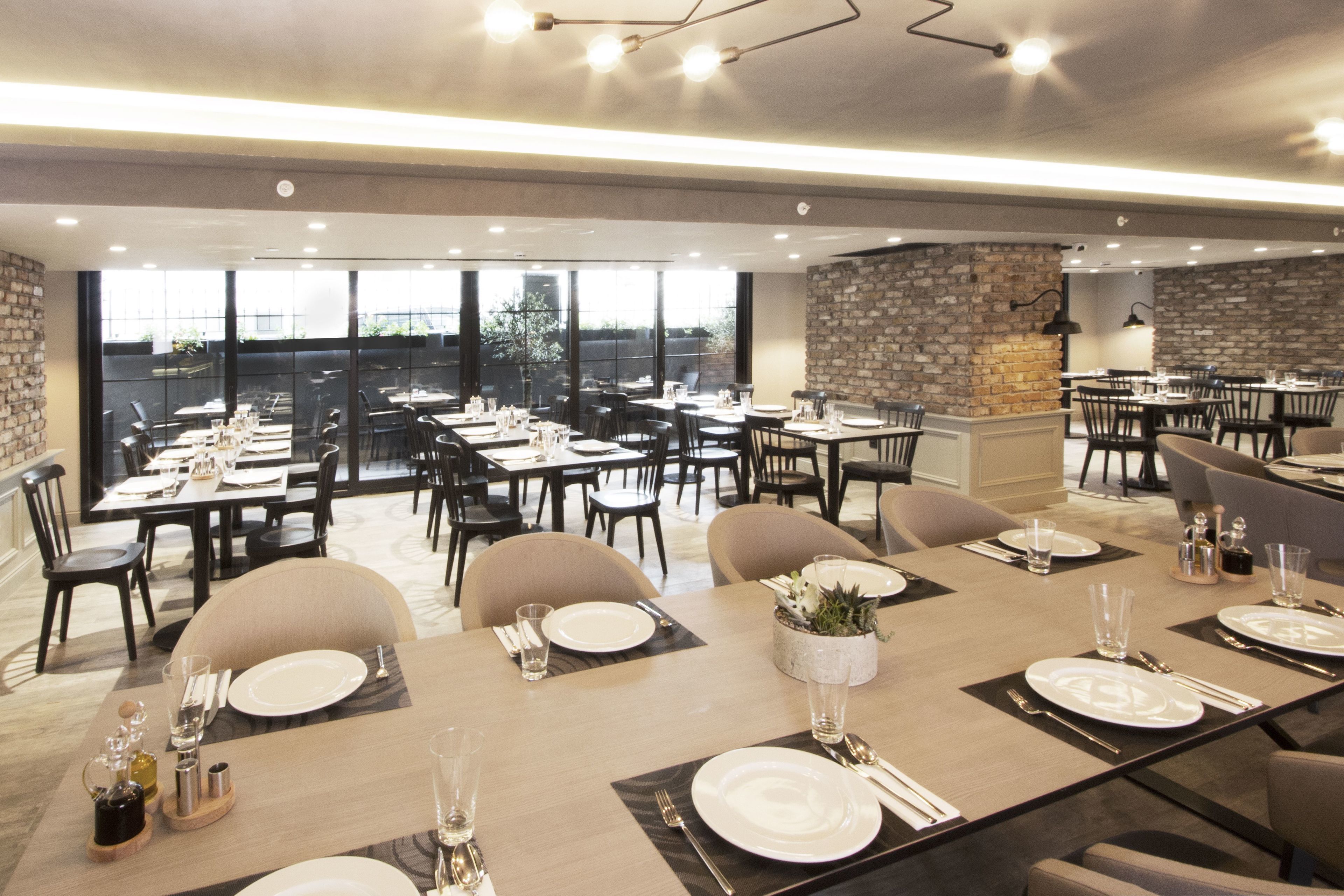A spacious dining area with multiple tables set for meals, large windows offering a view, and a stone accent wall.