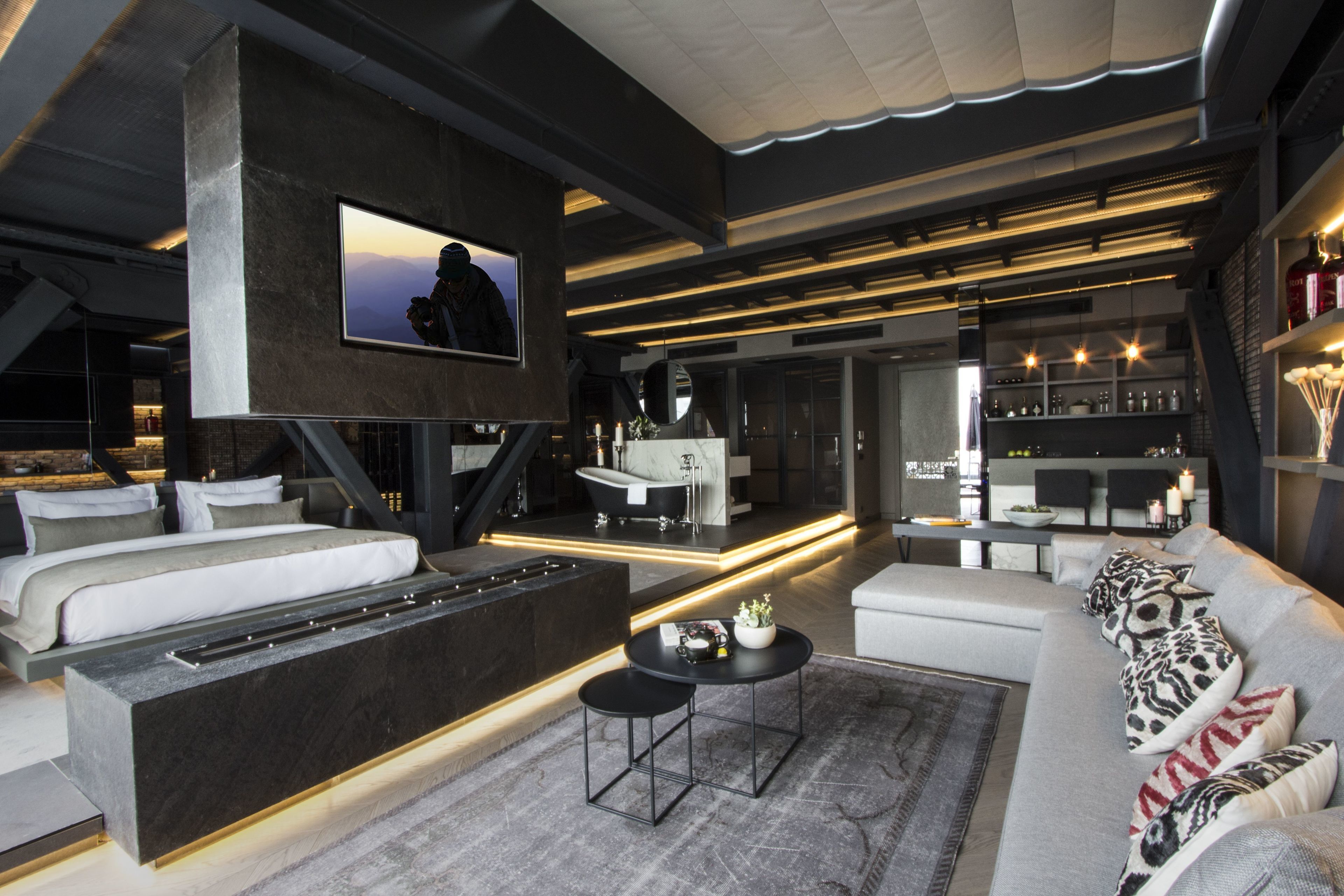 A modern living room with a sofa, a coffee table, a TV mounted on a wall, and a kitchen area in the background.