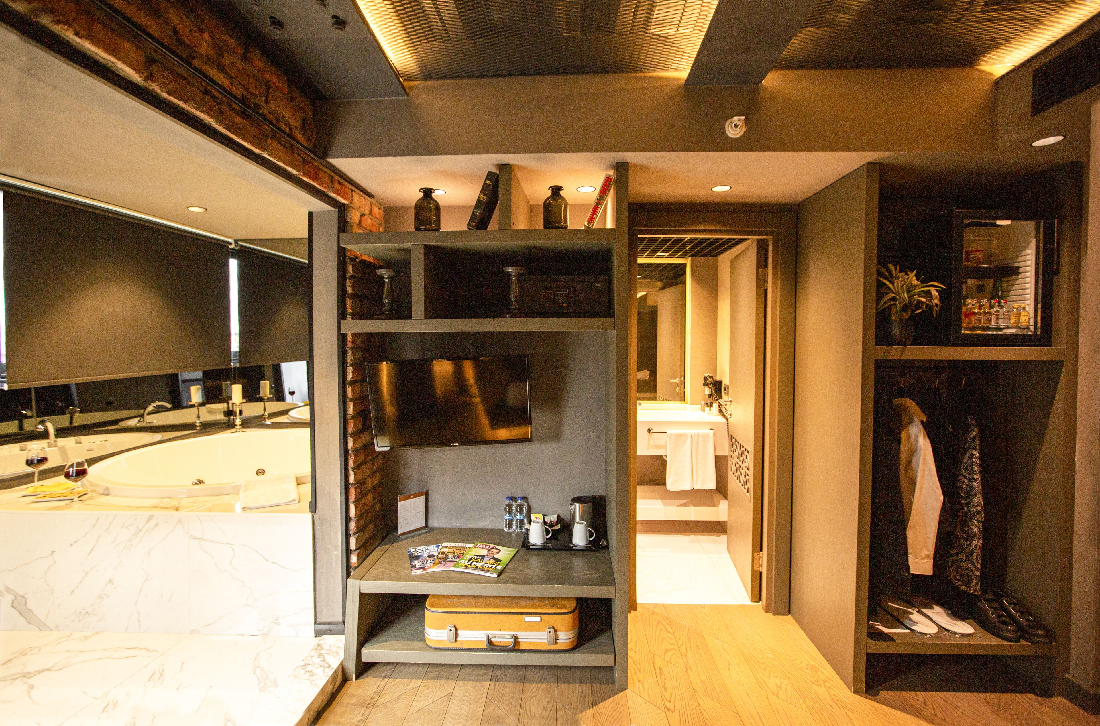 A modern bathroom with a marble countertop, a built-in sink, and a mirror above it. There is a shelf with toiletries and a suitcase on the floor.