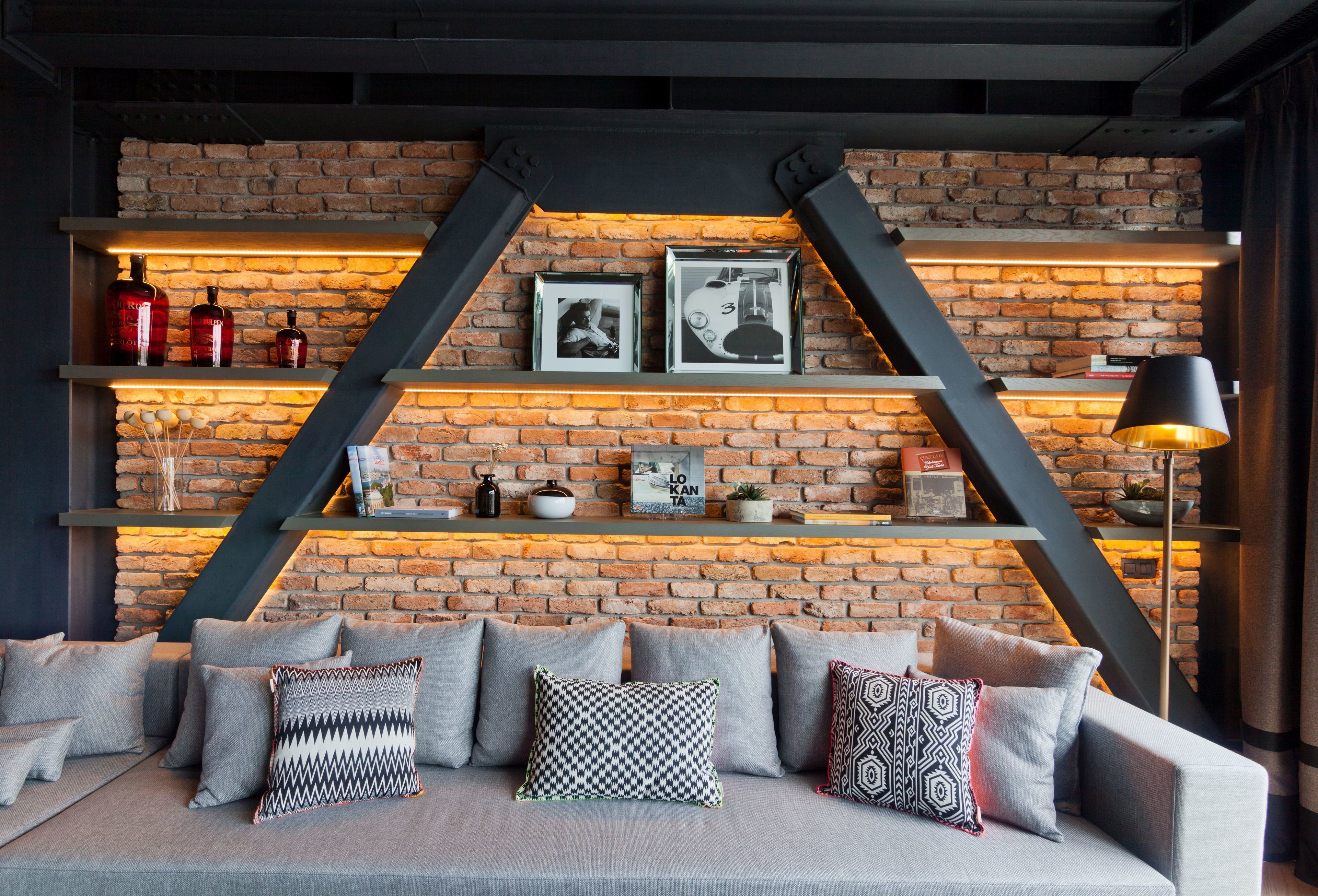 Un salon moderne avec un mur en briques, un canapé agrémenté de coussins à motifs et des étagères ornées d’objets décoratifs et de livres.