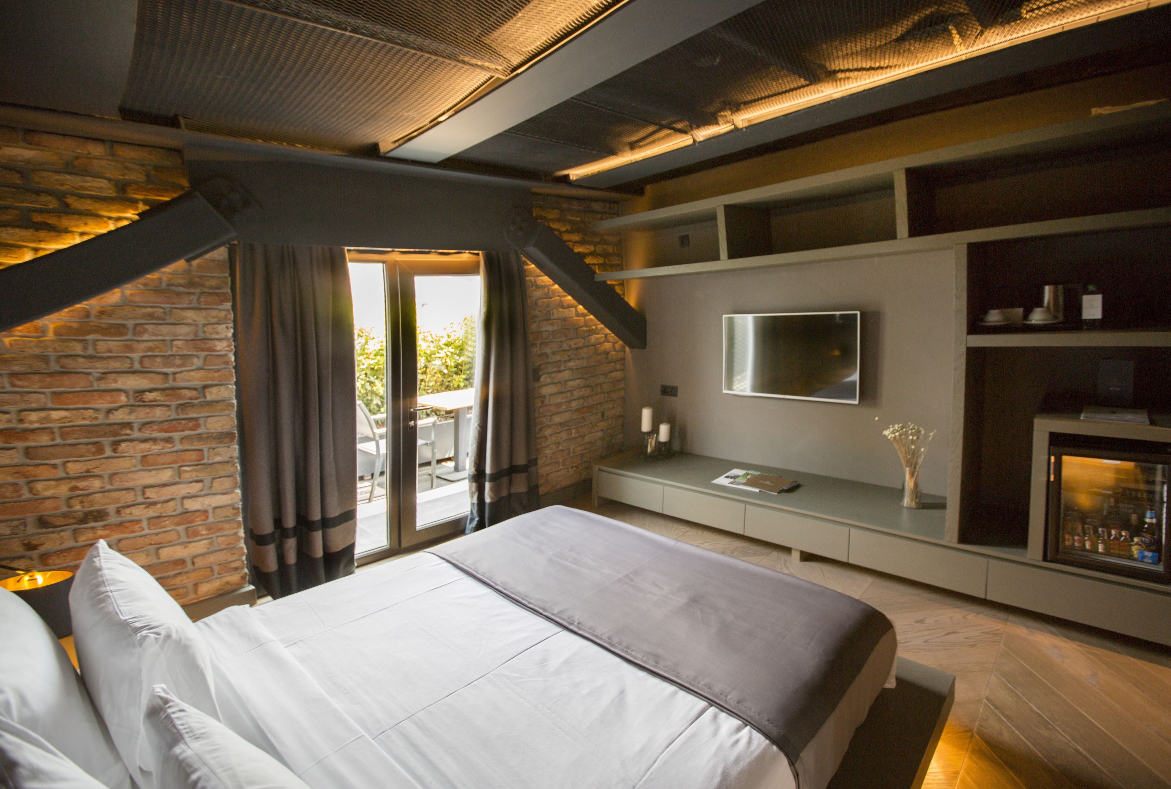 A modern bedroom with a large bed, a TV mounted on the wall, and a built-in minibar.