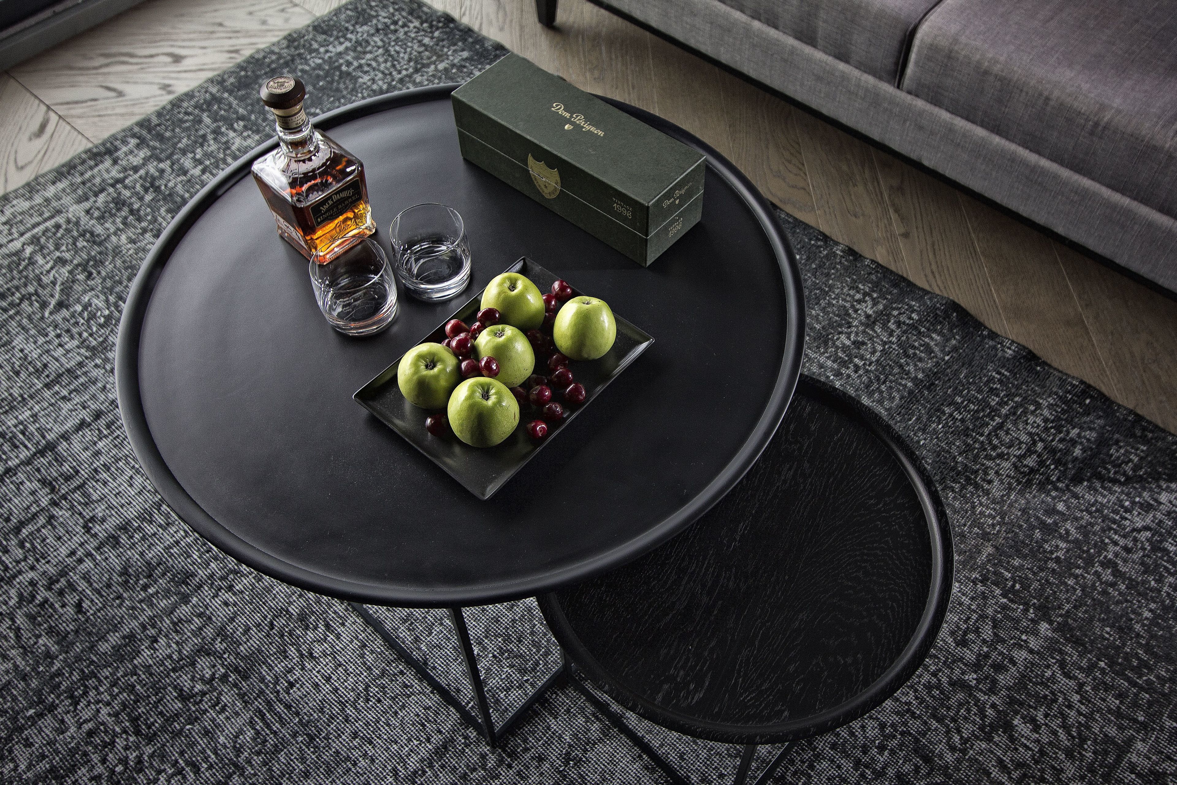 A round black table with a bottle of liquor, a glass, and a plate of green apples and red berries.