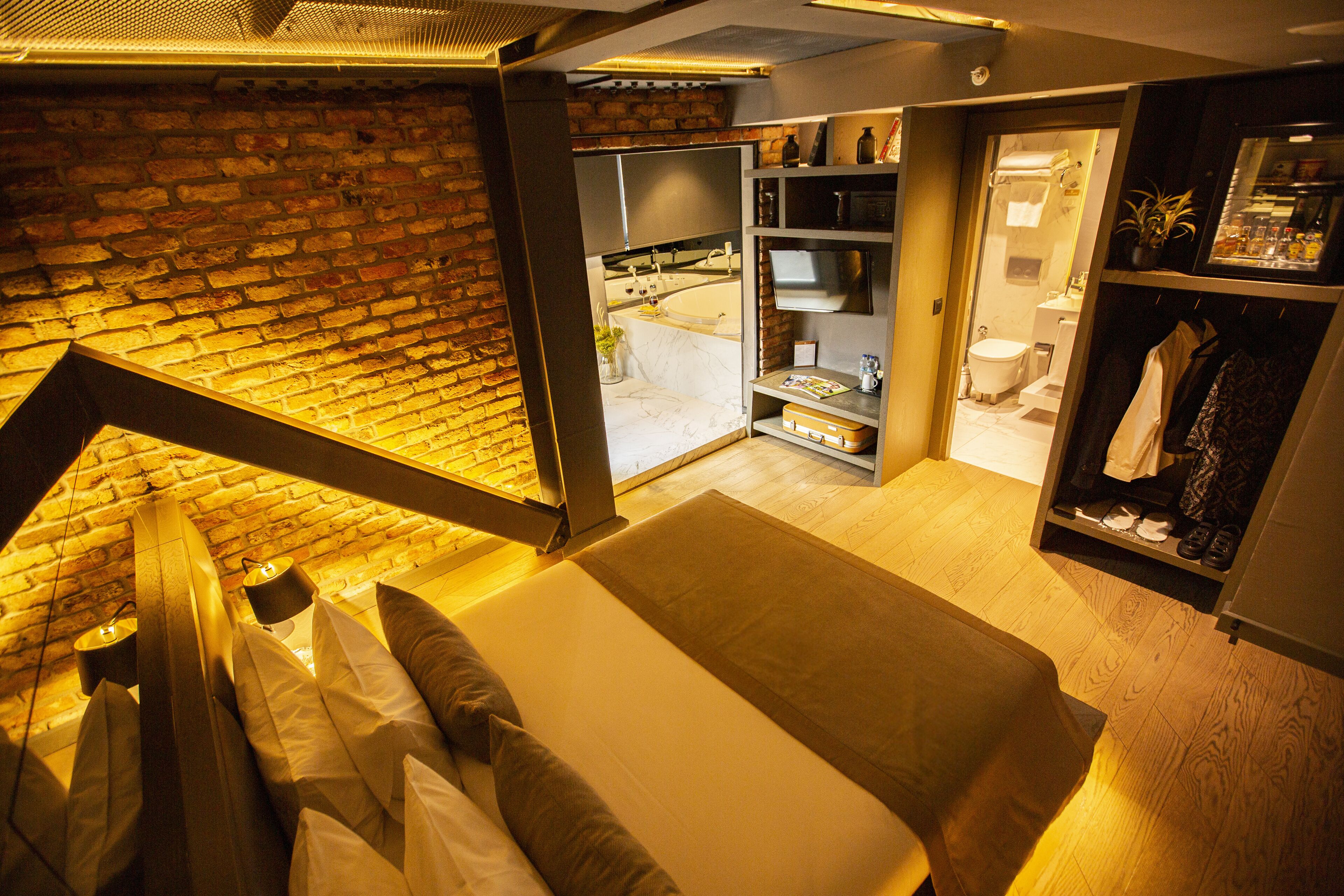 Ein modernes Schlafzimmer mit einem großen Bett, einer Ziegelwand und Blick auf ein Badezimmer.
