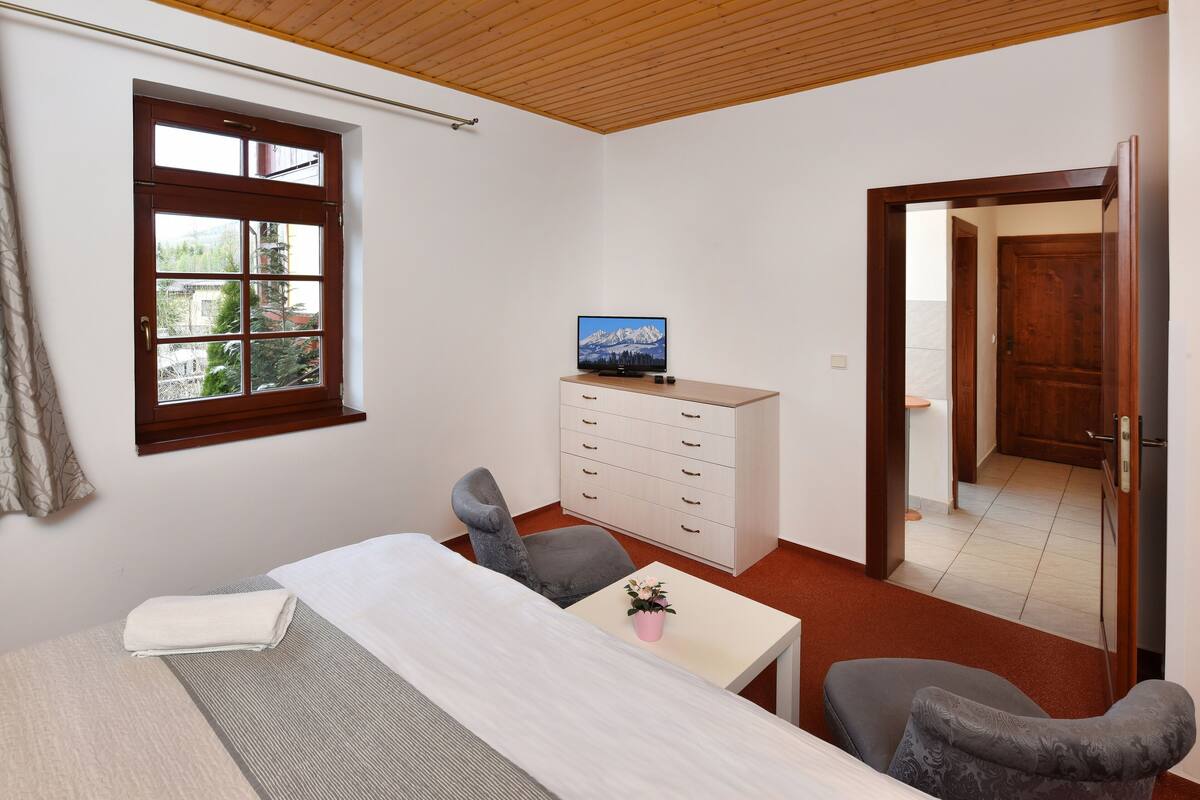 Ein Schlafzimmer mit Bett, Schreibtisch, Stuhl, Kommode, Fernseher und einem Fenster mit Bergblick.