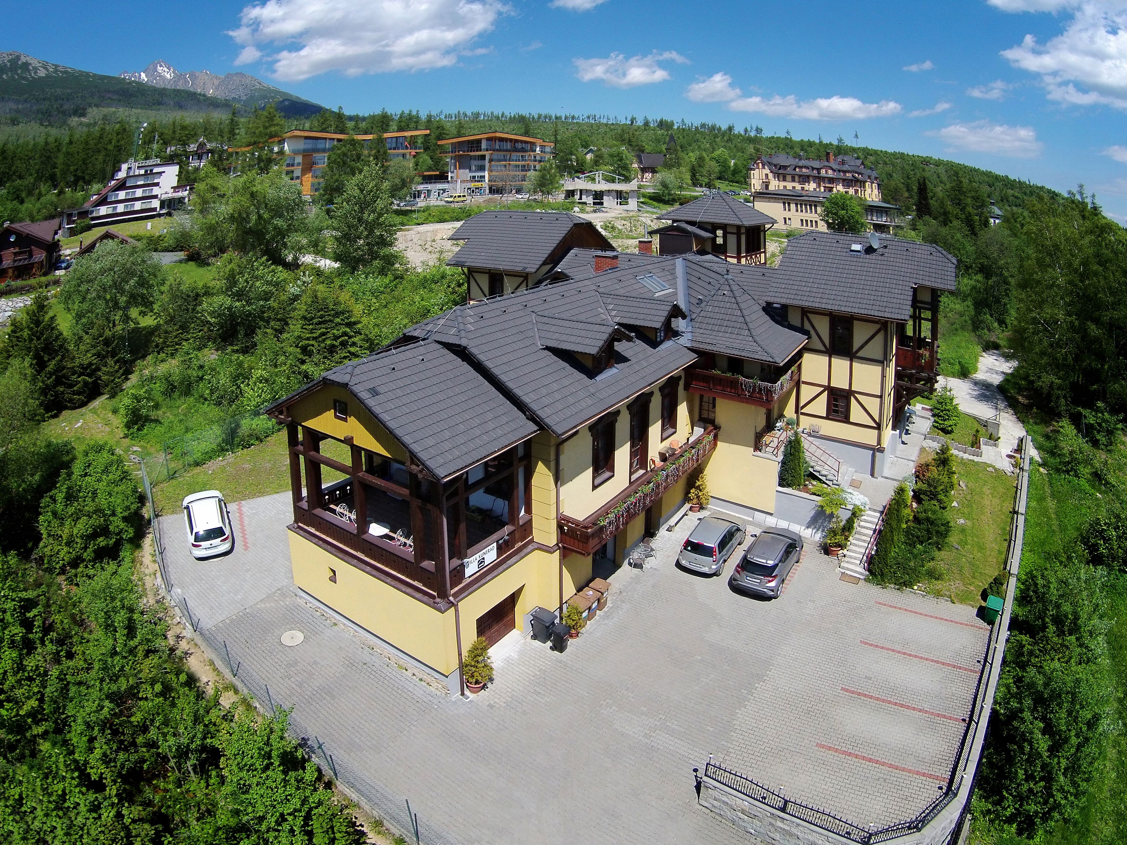 Ein mehrstöckiges Hotel mit Parkplatz, umgeben von Grünflächen und Bergen im Hintergrund.