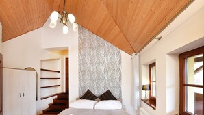 A bedroom with a wooden ceiling, a bed with white linens, a wardrobe, a patterned wallpaper, and a window with a view. - Villa Kunerad (Vysoké Tatry)