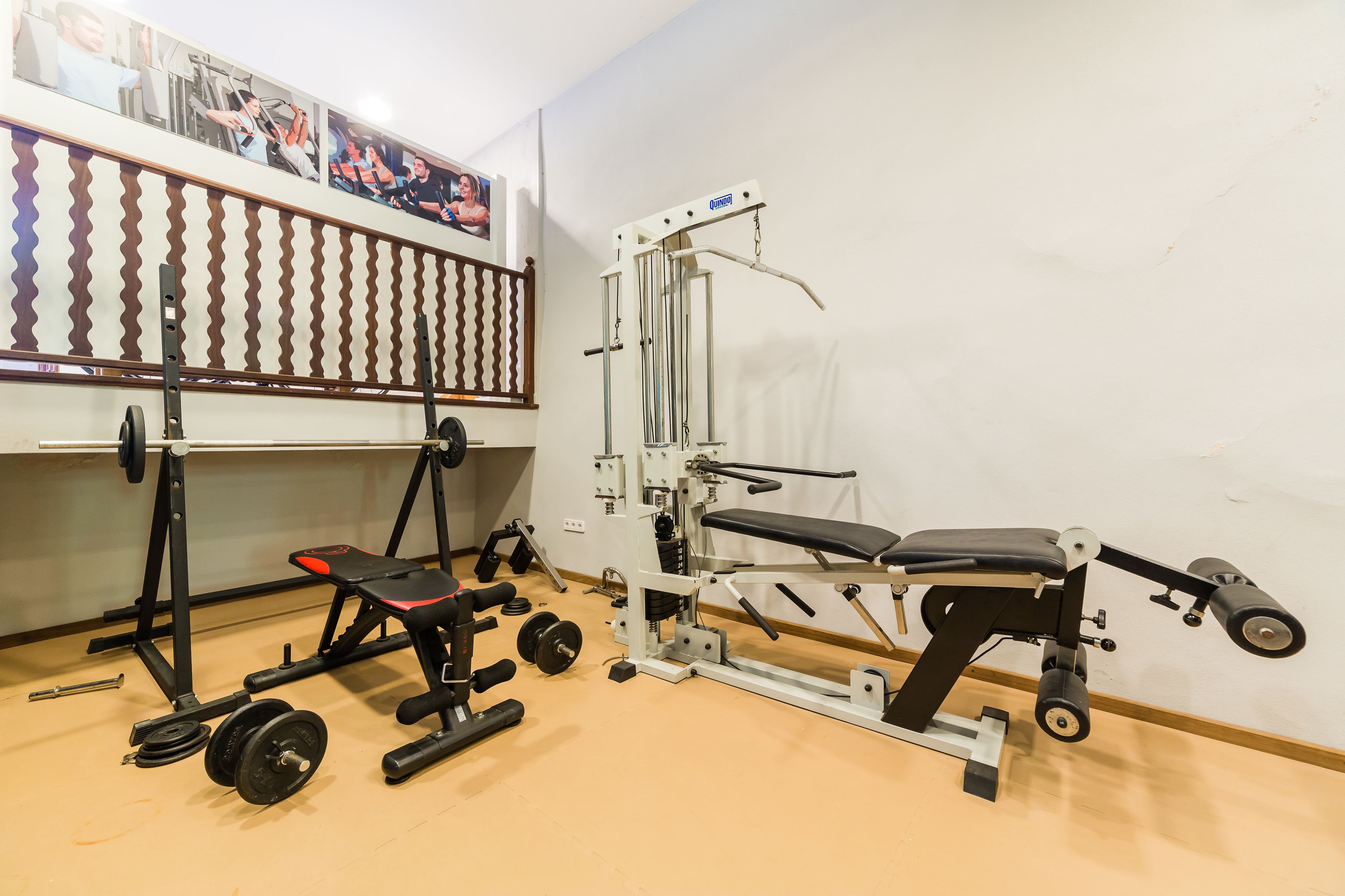 Un gimnasio con equipo de ejercicio variado, incluyendo una prensa de banca, un rack de sentadillas y discos de pesas.