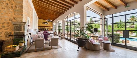 A spacious lobby with a stone wall, wooden ceiling beams, and large windows offering a view of the outdoors.