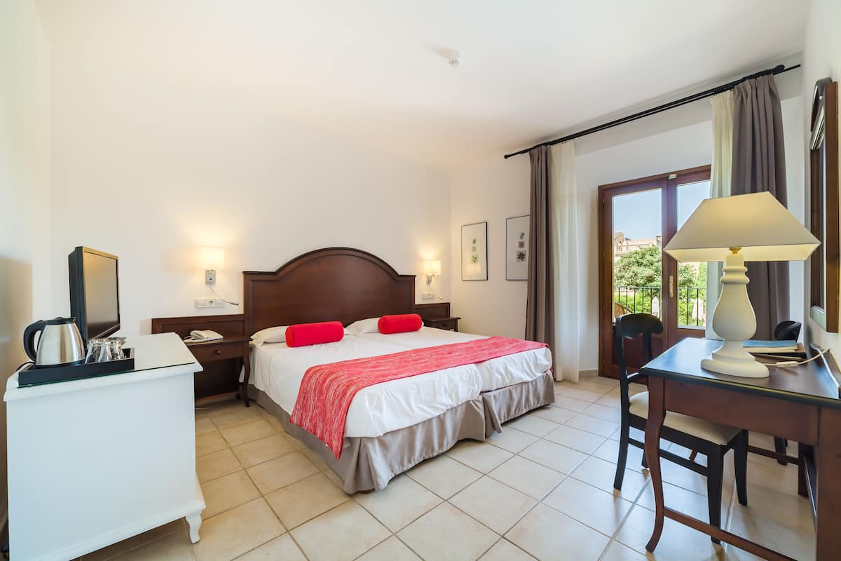 A hotel room with a bed, bedside table, lamp, and a view of the outdoors.