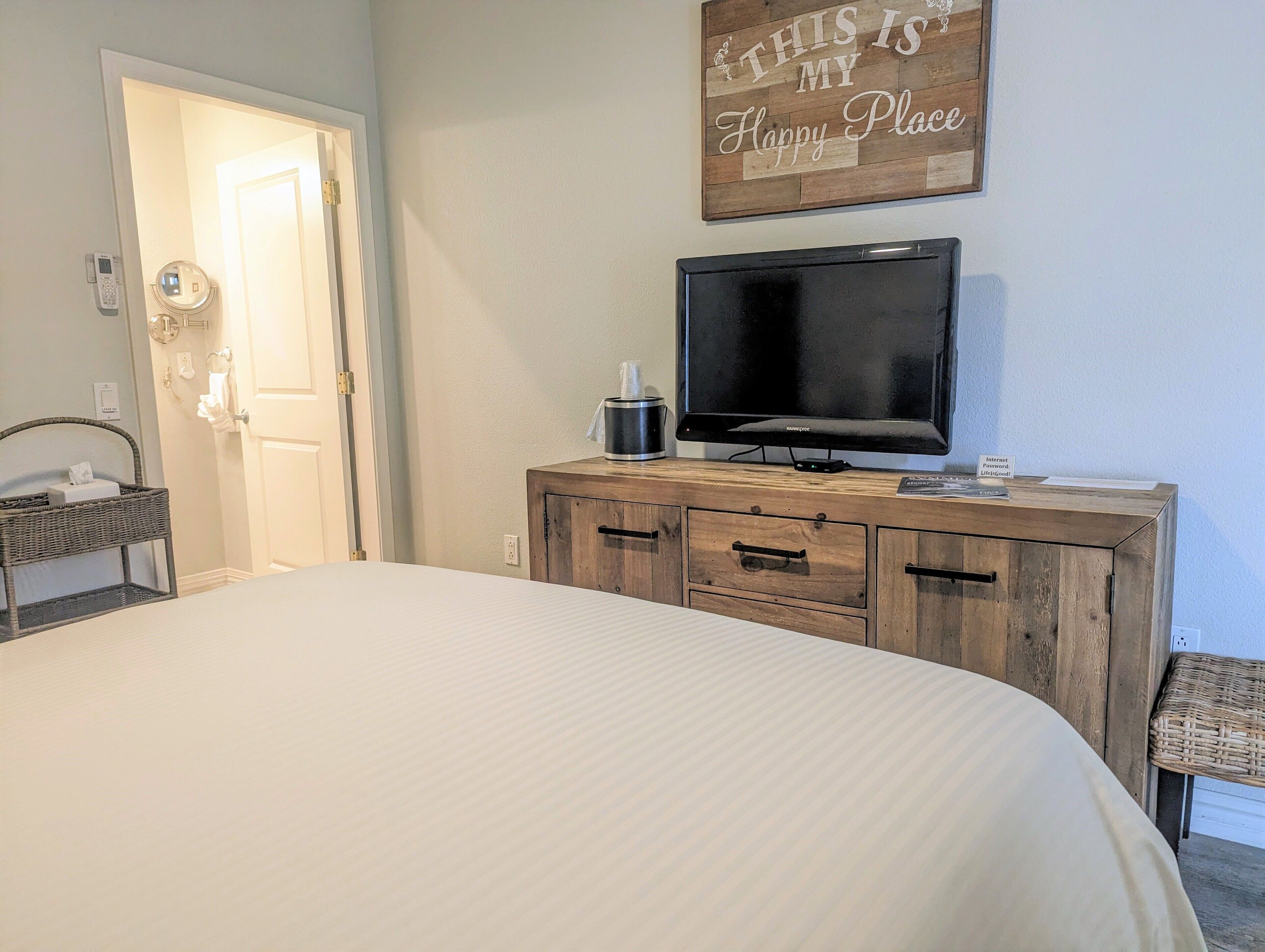 Une chambre à coucher avec un lit, une commode en bois, un téléviseur et un panneau décoratif mural.