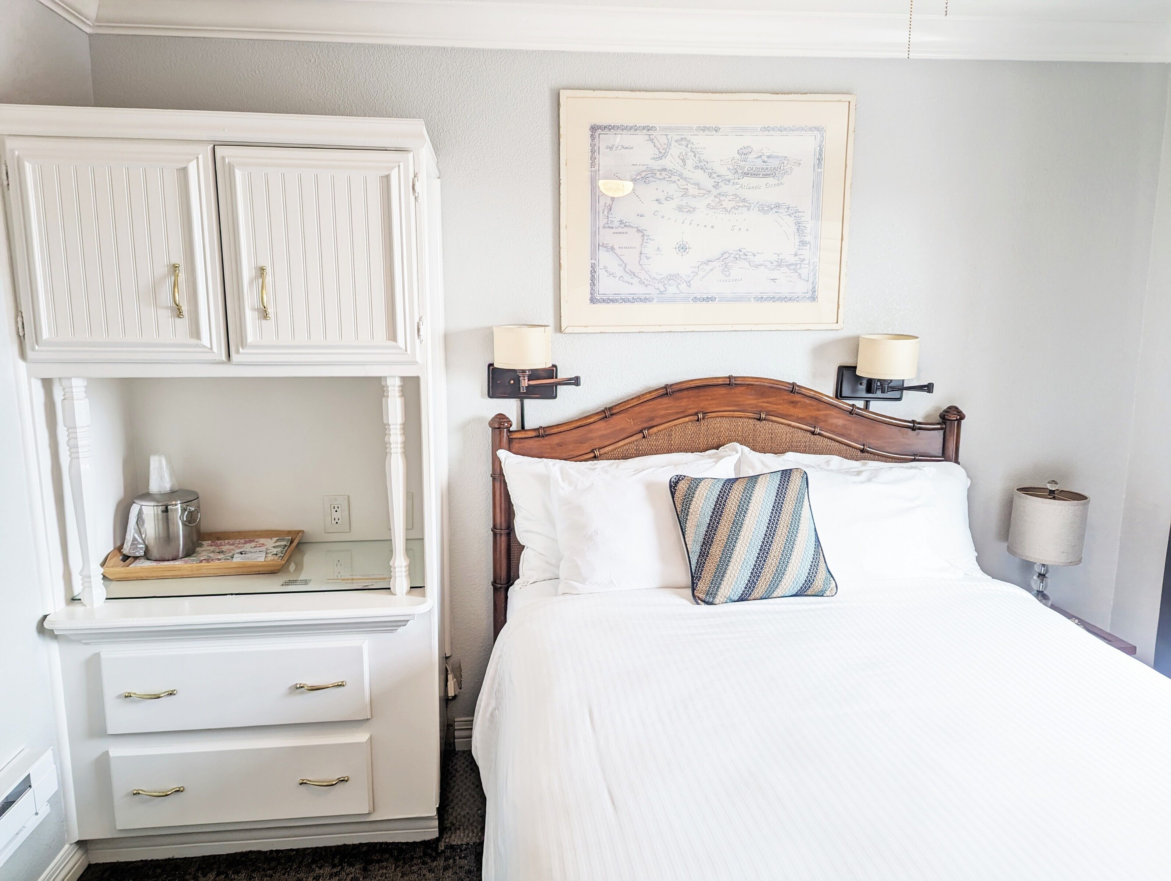 Une chambre à coucher bien rangée, avec un lit en bois, des tables de chevet blanches et une carte accrochée au mur.