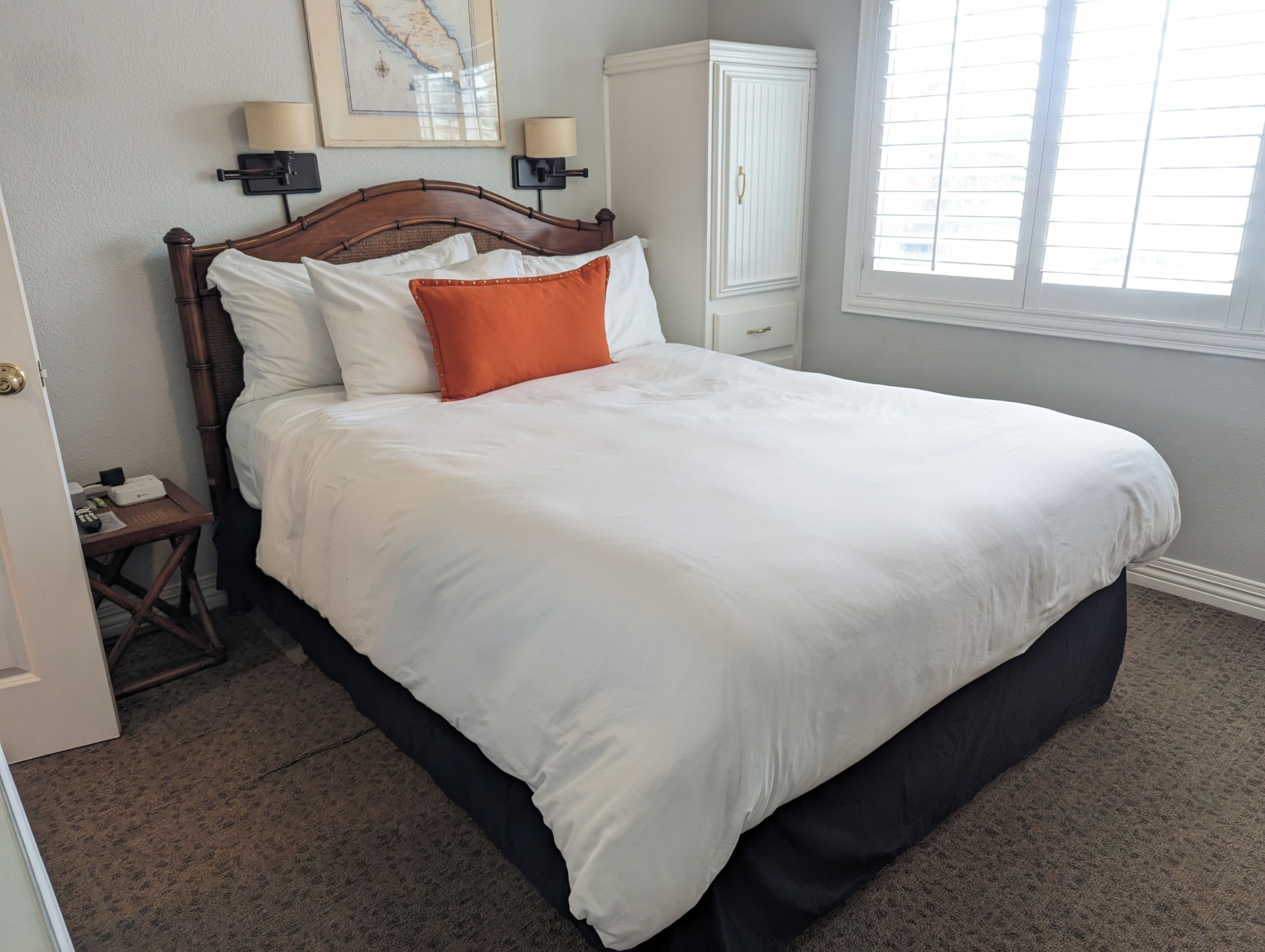 A neatly made bed with white and orange pillows, a wooden headboard, and a nightstand with a lamp.
