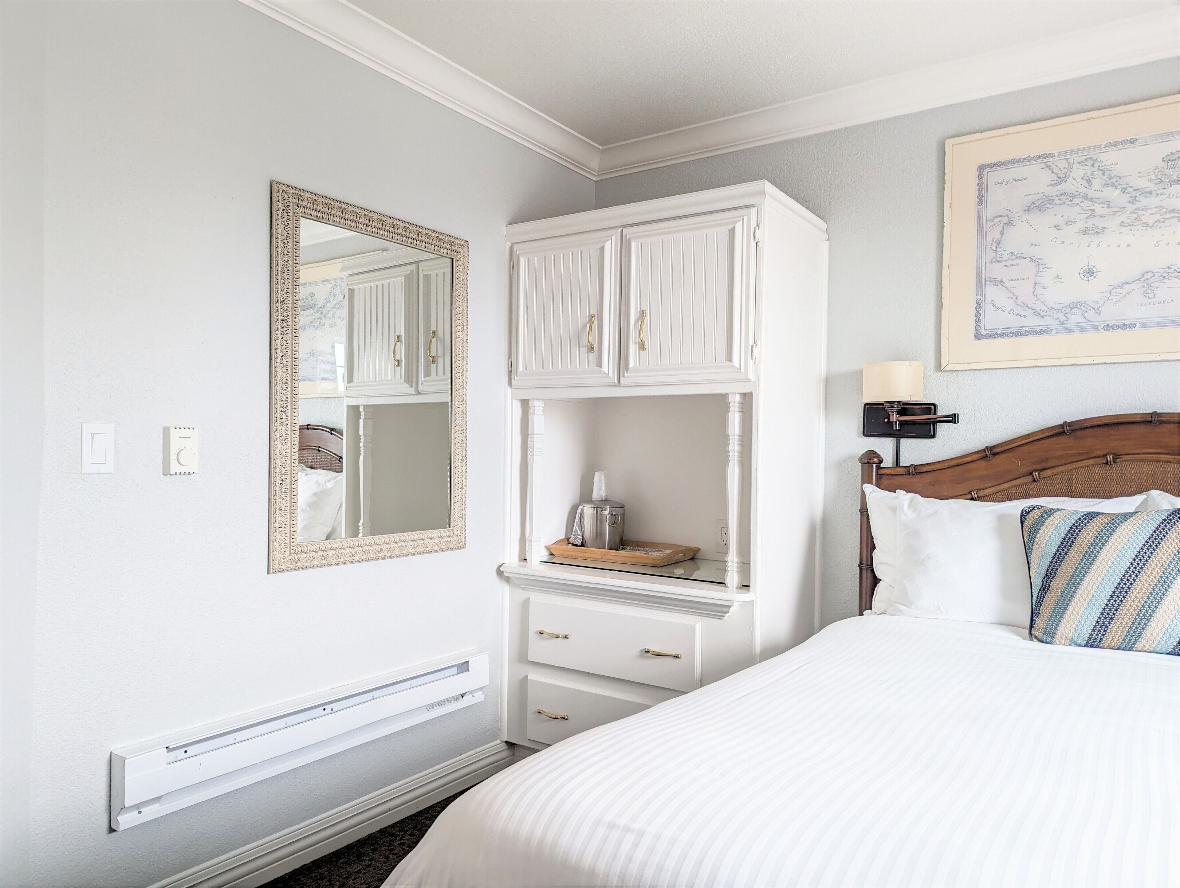 Un dormitorio con cama, cómoda, espejo, un mapa en la pared y termostato.