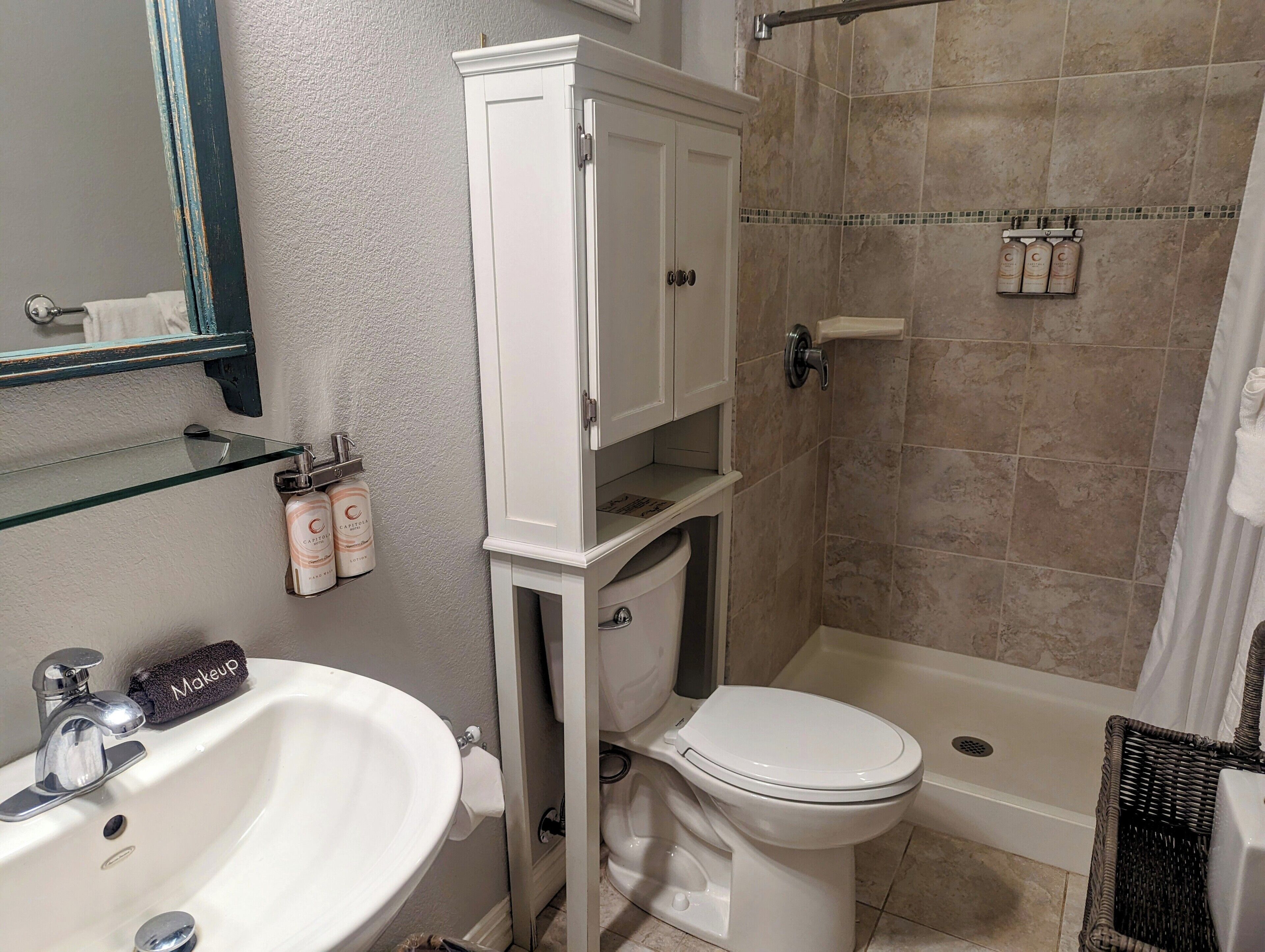 A bathroom with a white sink, toilet, and shower area. There are toiletries on the wall and a towel rack.