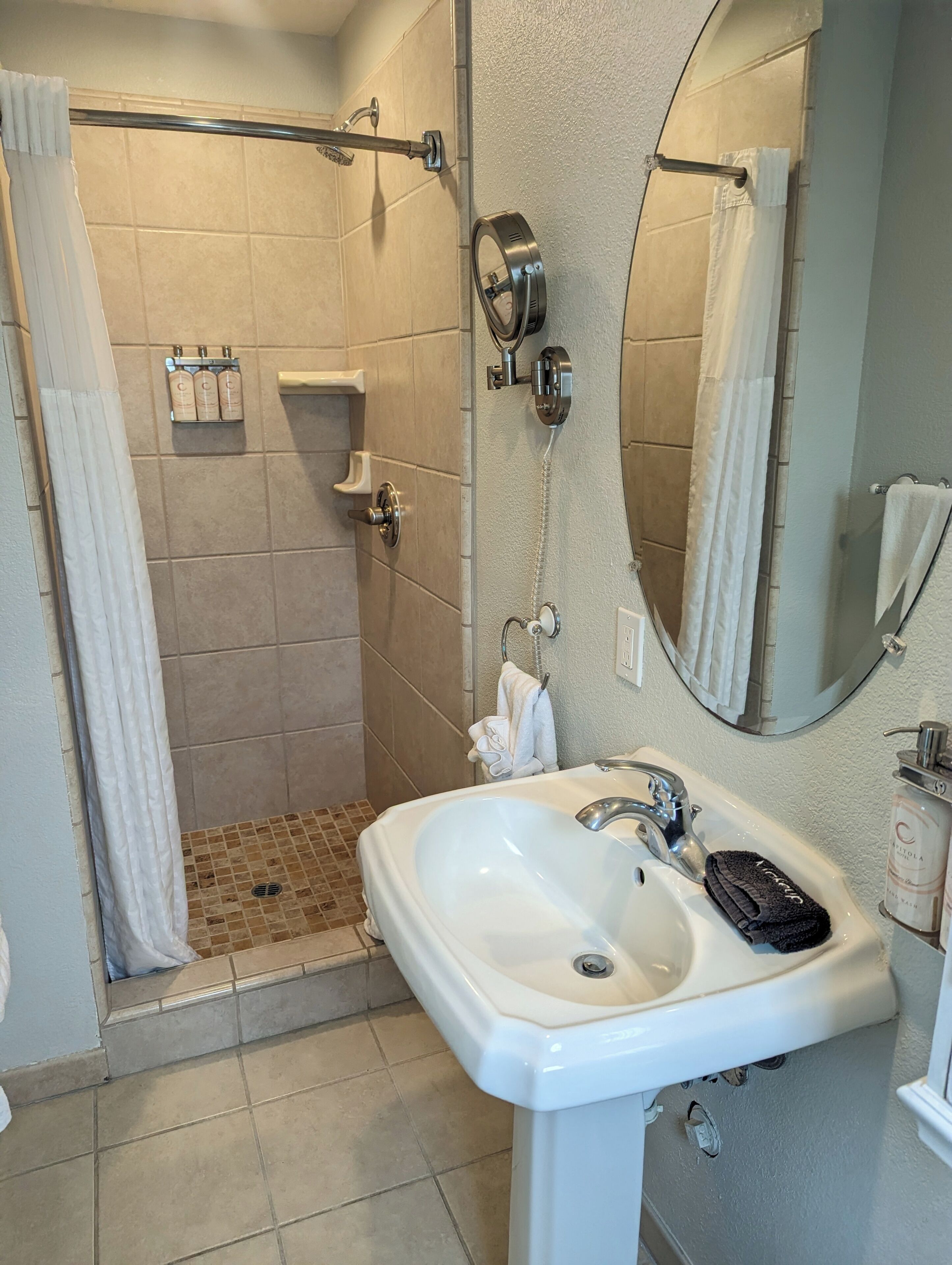 A bathroom with a shower, a sink, a mirror, and a towel rack.