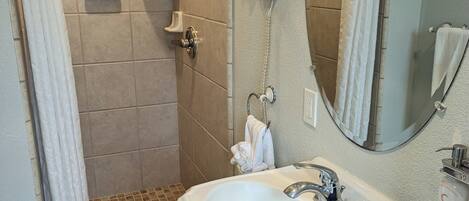 Un baño con ducha, lavamanos, espejo y toallero.