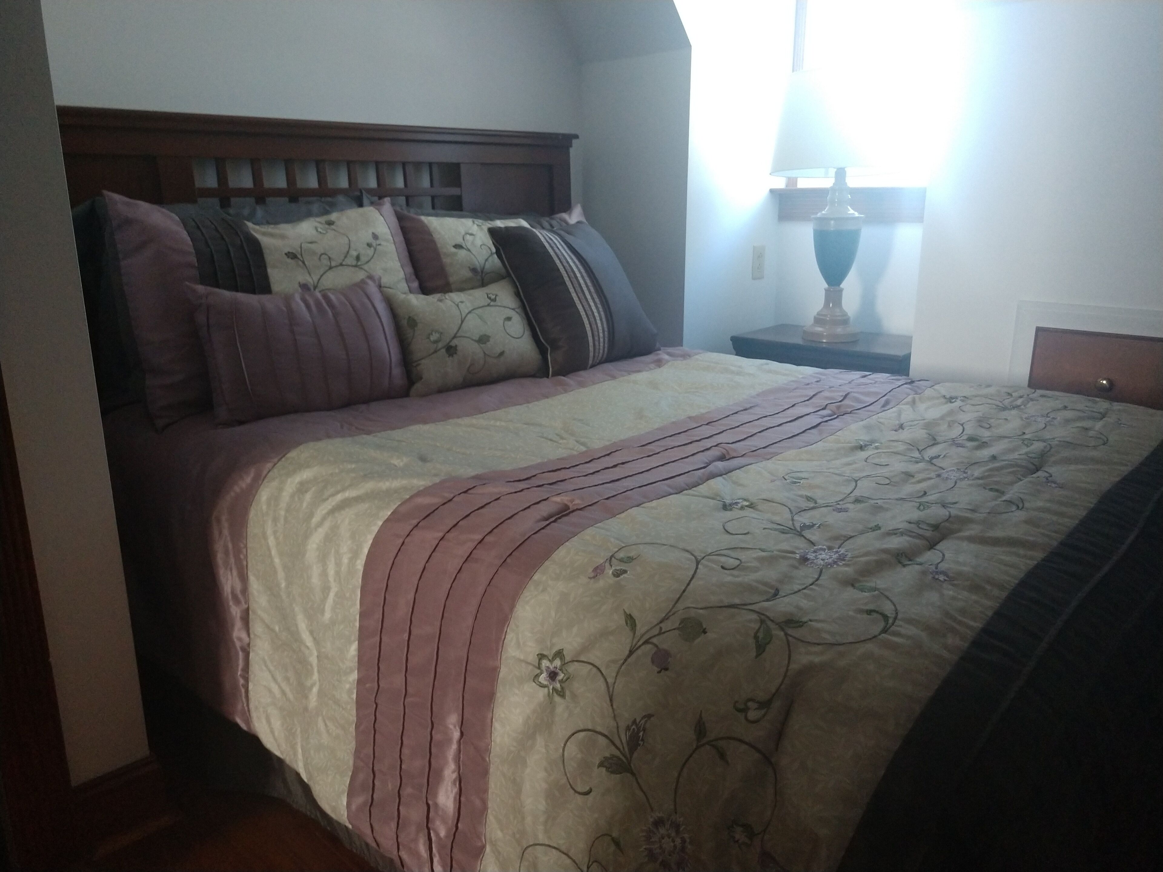 A neatly made bed with a wooden headboard, multiple pillows, and a bedside table with a lamp.
