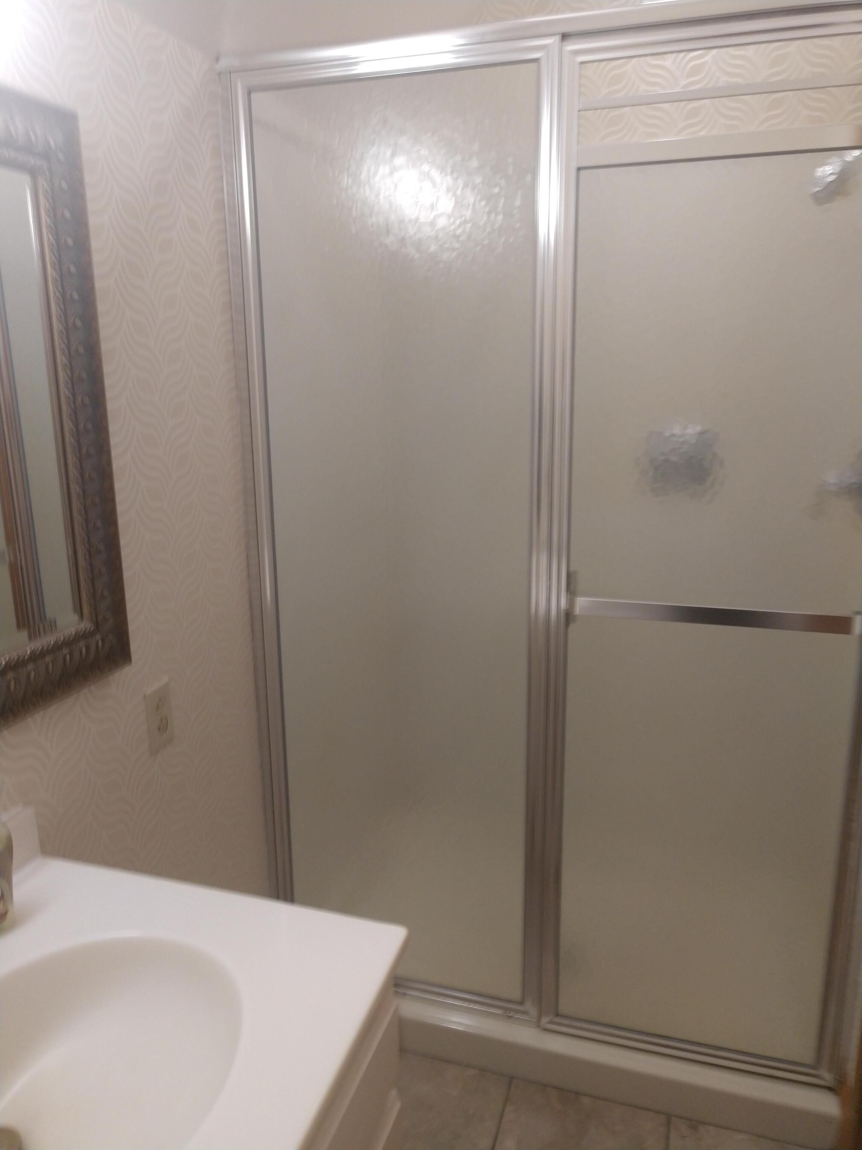 A bathroom with a shower enclosure, a sink, and a mirror.