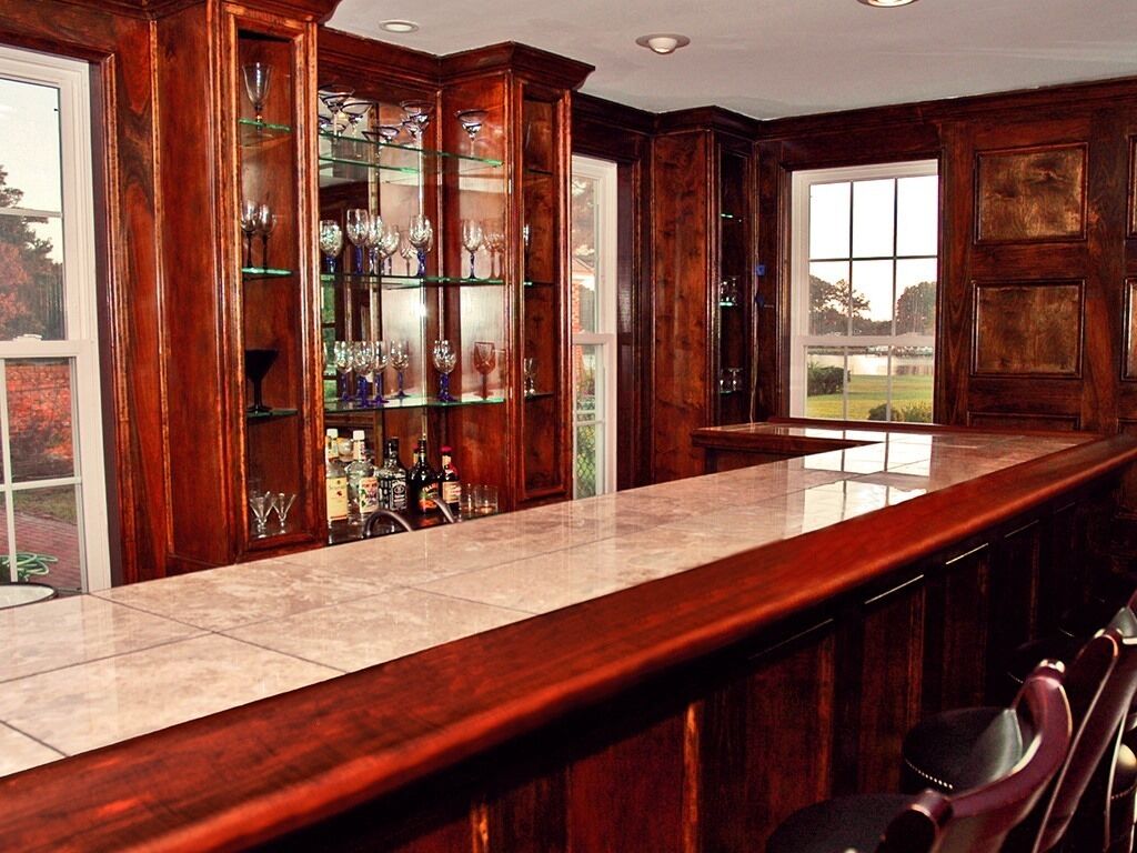 A bar area with a wooden counter and glass display cabinets filled with bottles and glasses.