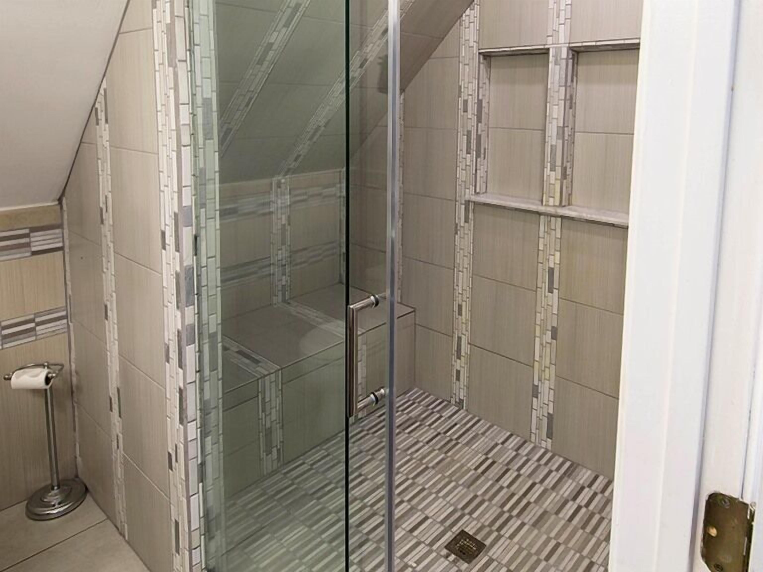 A glass-enclosed shower with tiled walls and floor, a towel rack, and a toilet.