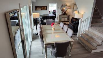 A dining area with a table, chairs, and a vase of flowers. There is a piano and a mirror in the background.