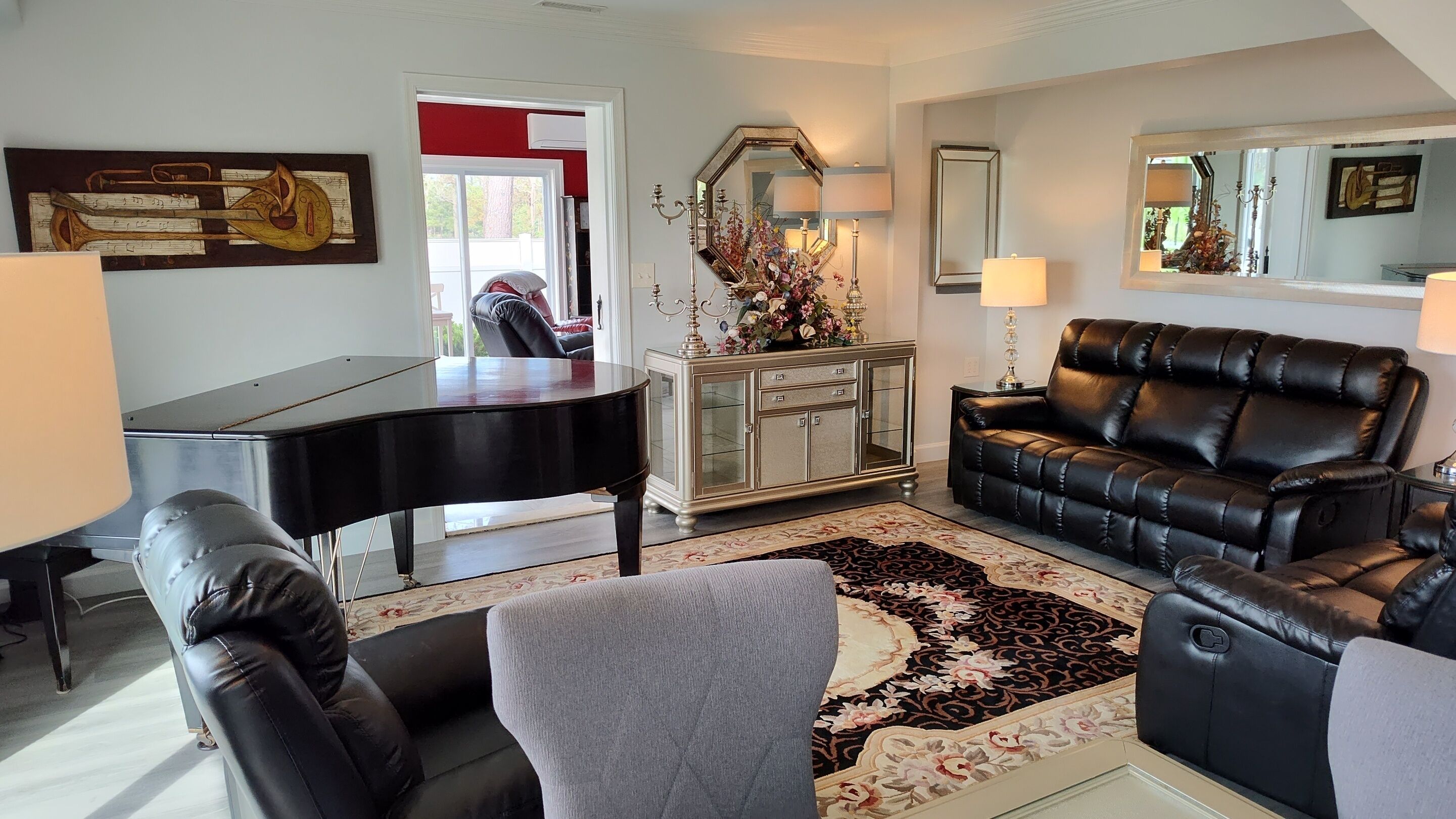 A living room with a grand piano, a black leather sofa, a grey armchair, and a decorative cabinet.