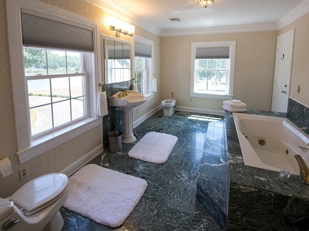 Une salle de bain avec un sol en marbre, une baignoire, un lavabo et deux fenêtres.
