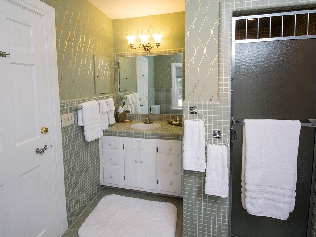 A bathroom with a white door, a sink with a mirror above it, and a towel rack with multiple towels.