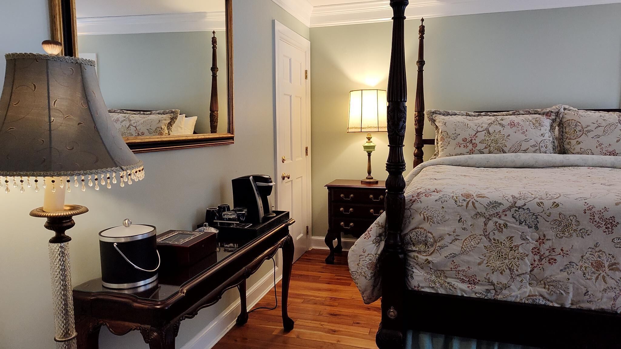 Un dormitorio con cama con dosel, una mesita de noche con lámpara, un tocador y un espejo en la pared.
