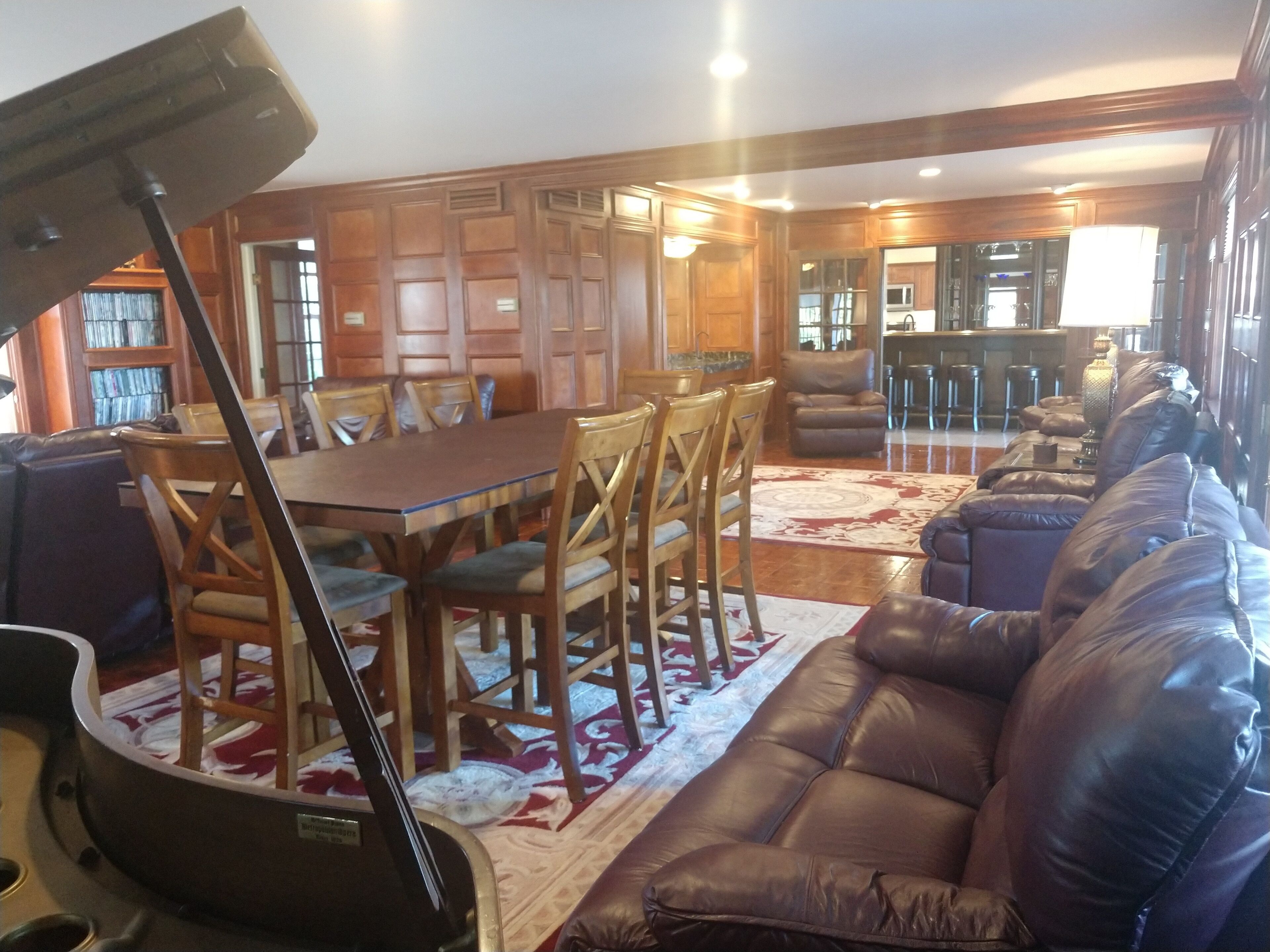 A spacious living room with a large brown leather sofa, wooden dining table with chairs, and a kitchen area in the background.