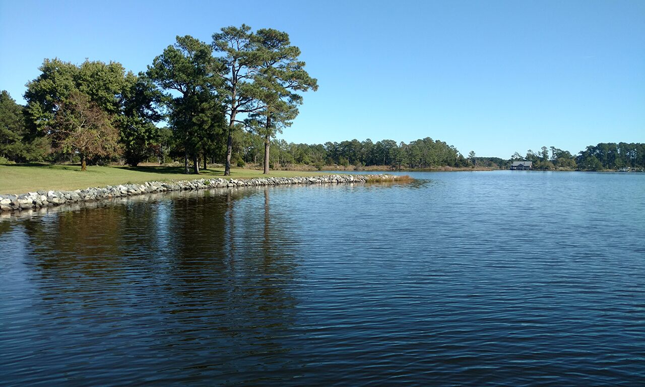 Un lago tranquilo con un muro de piedra y árboles a la izquierda.