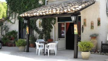 An outdoor patio with a tiled roof, a table with chairs, and potted plants.