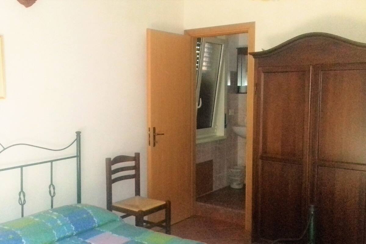 Une chambre à coucher comprenant un lit, une armoire en bois, une chaise et une porte donnant sur une salle de bain.