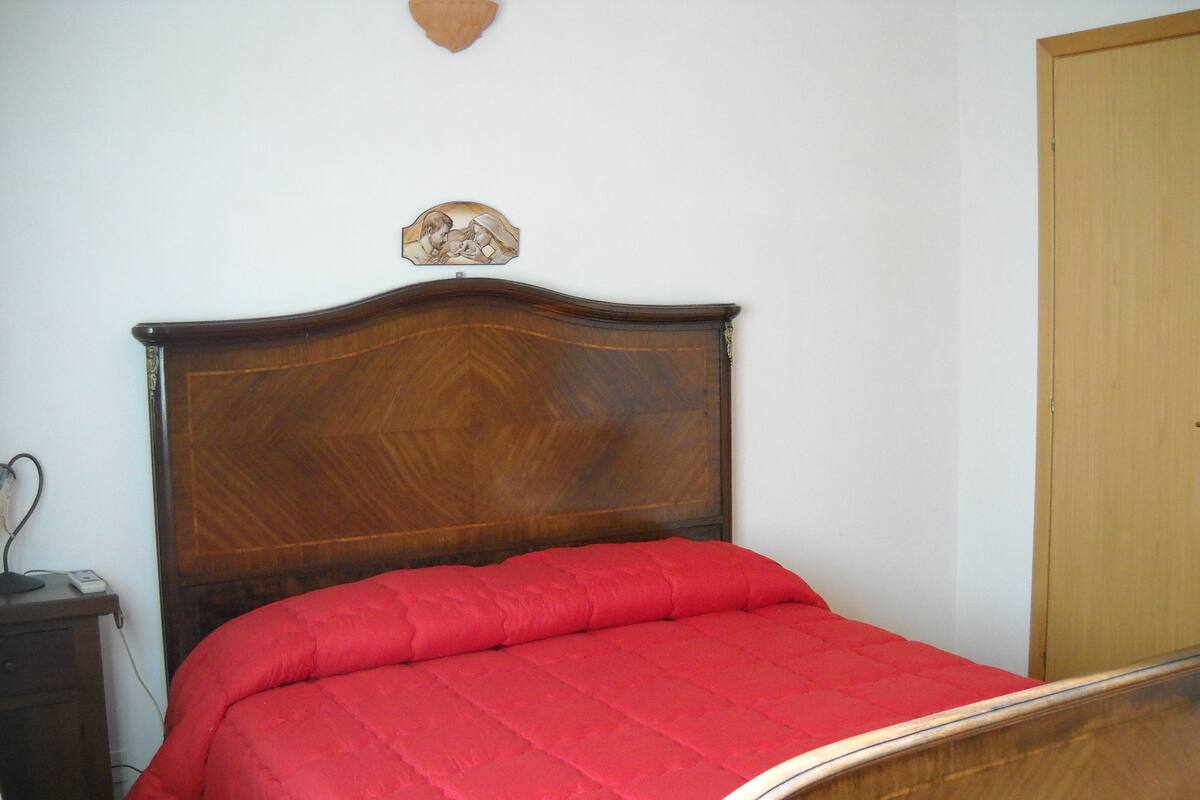 Une chambre à coucher avec une tête de lit en bois, une couvre-lit rouge, un luminaire fixé au mur et une porte en bois.