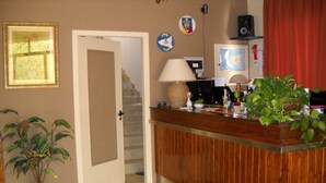 A reception area with a wooden counter, a potted plant, a door leading to a staircase, and a wall with various decorations.