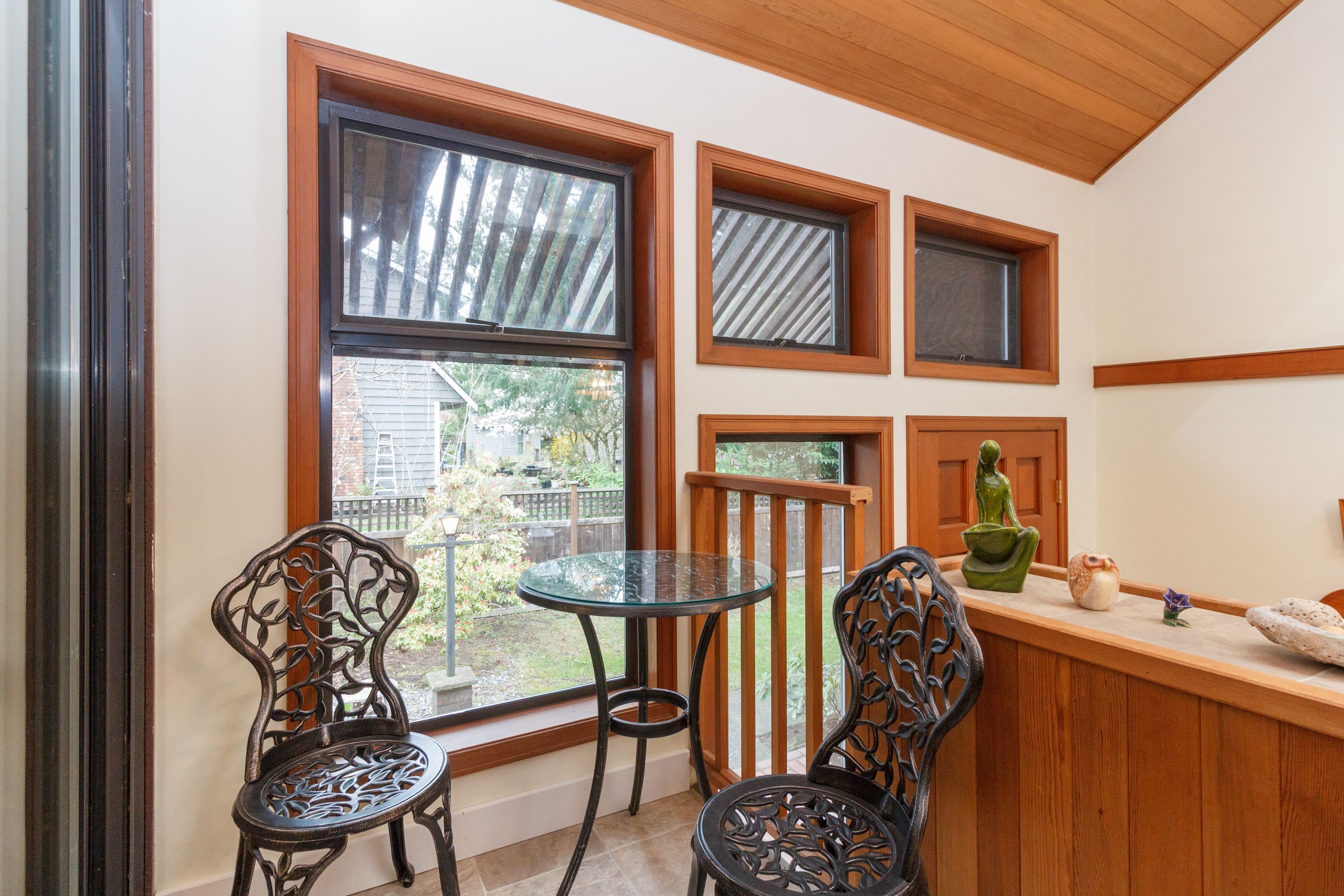 A small room with a glass table and two chairs, a wooden bench, and a window with a view of a backyard.